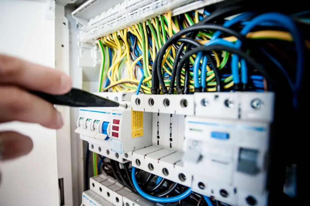 Armoire-elec Hand of electrician working on a circuit breaker panel with colorful wires, ensuring safe electrical connections.