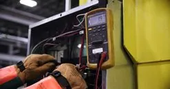 Les domaines de tension. Electrician using a multimeter to fix industrial control panel wiring.